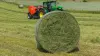 Nice round silage bale with net binding and a KUHN FB 3130 fixed round baler on the background.